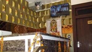 A hotel lobby with a marble reception desk, a television mounted on the wall, a ceiling fan, and a door labeled "101". - Dashrath Residency (Ayodhya)