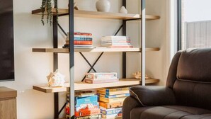 Una sala de estar moderna con un sofá de cuero marrón, una mesa de centro de madera y una estantería llena de libros y juegos de mesa.