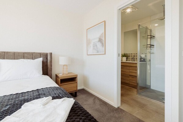 Een slaapkamer met een bed, nachtkastje, lamp en een ingelijst beeld aan de muur.