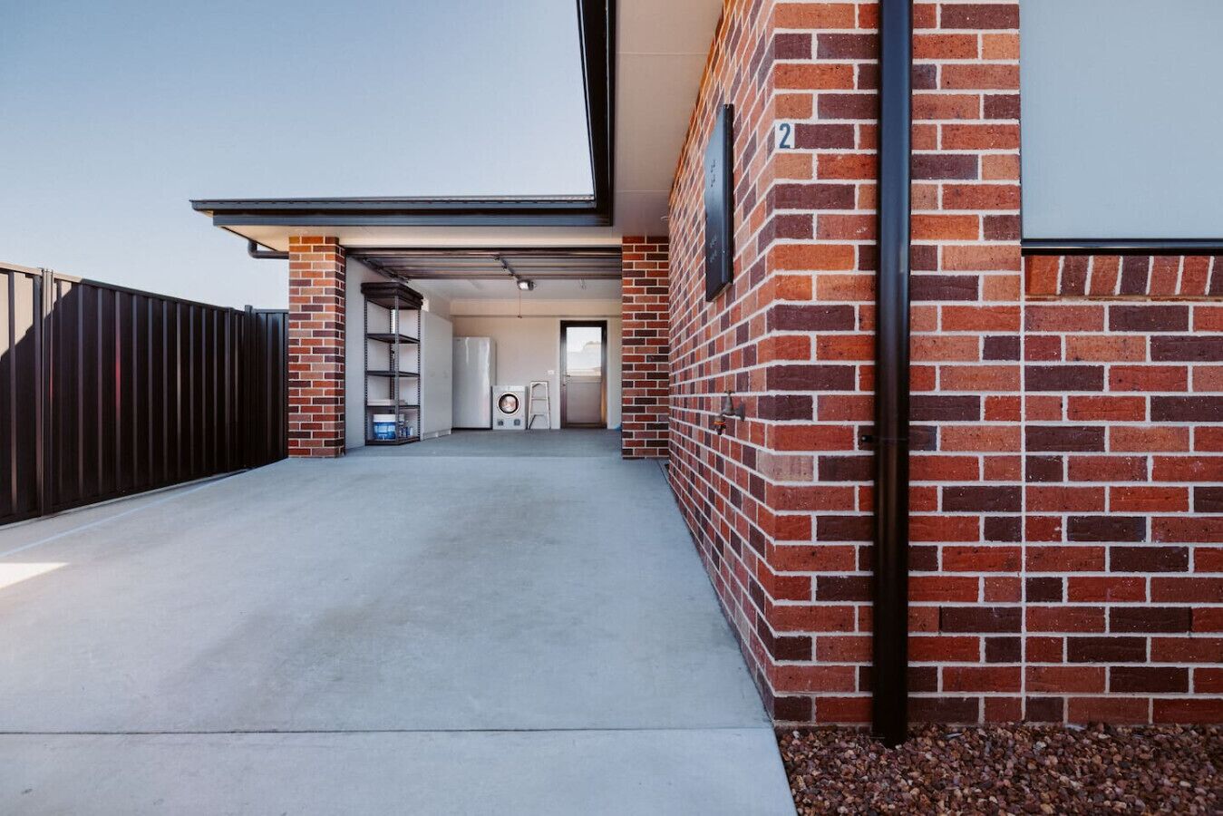 A modern building with a brick exterior, a metal gate, and a concrete driveway leading to a door.