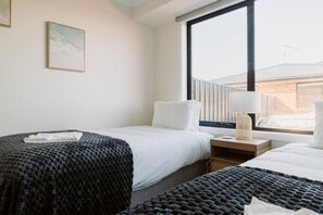 Een hotelkamer met twee bedden, een groot raam, een nachtkastje met een lamp en uitzicht op een gebouw.