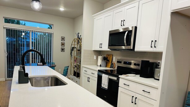 A modern kitchen with white cabinets, a stainless steel sink, a black microwave, and a black dishwasher. - Charming townhome with AC in Hillsboro (Hillsboro)