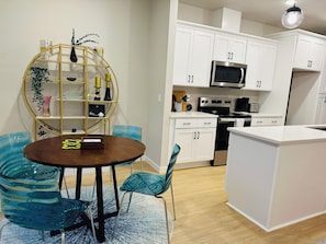 A modern kitchen with white cabinets, a microwave, and a stove. There is a dining area with a round table and chairs.