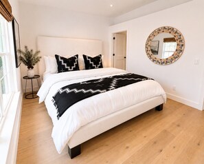 A bedroom with a bed, a round mirror, and a small table with a plant.