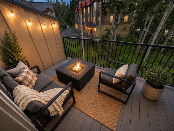 A deck with outdoor seating, a fire pit, and a railing overlooking a residential area.