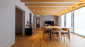 Un interno moderno con pavimento in legno, una zona pranzo con tavolo e sedie, e ampie finestre che lasciano entrare luce naturale.