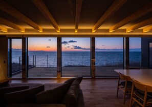 A spacious room with a large sliding glass door leading to a deck with a view of the sea and mountains. - Yunagi  (Ishikari)
