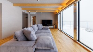 Un soggiorno moderno con un ampio divano componibile, travi in legno a soffitto e una grande finestra che offre vista sull'esterno.