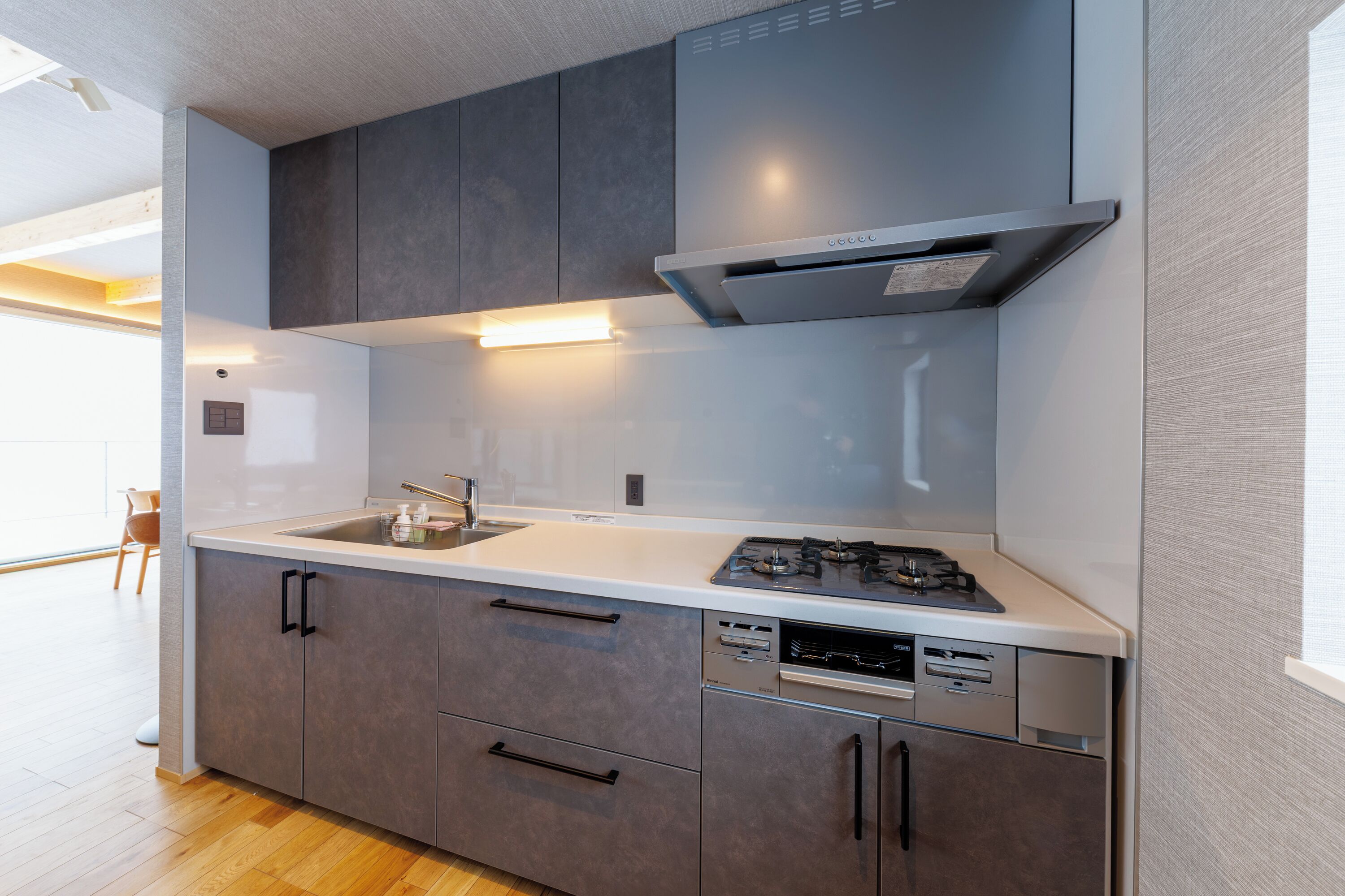 A modern kitchen with grey cabinets, a white countertop, a built-in dishwasher, and a gas stove.