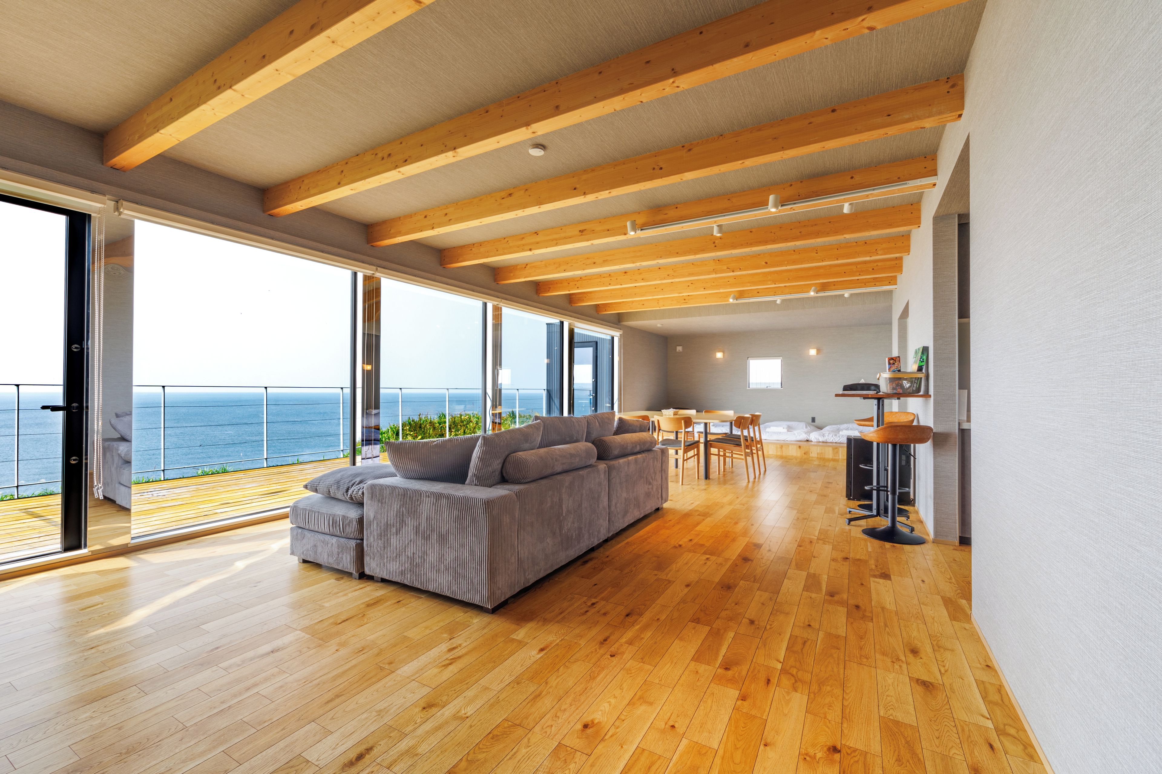 Een ruime woonkamer met een grote bank, houten vloeren en uitzicht op zee door grote ramen.