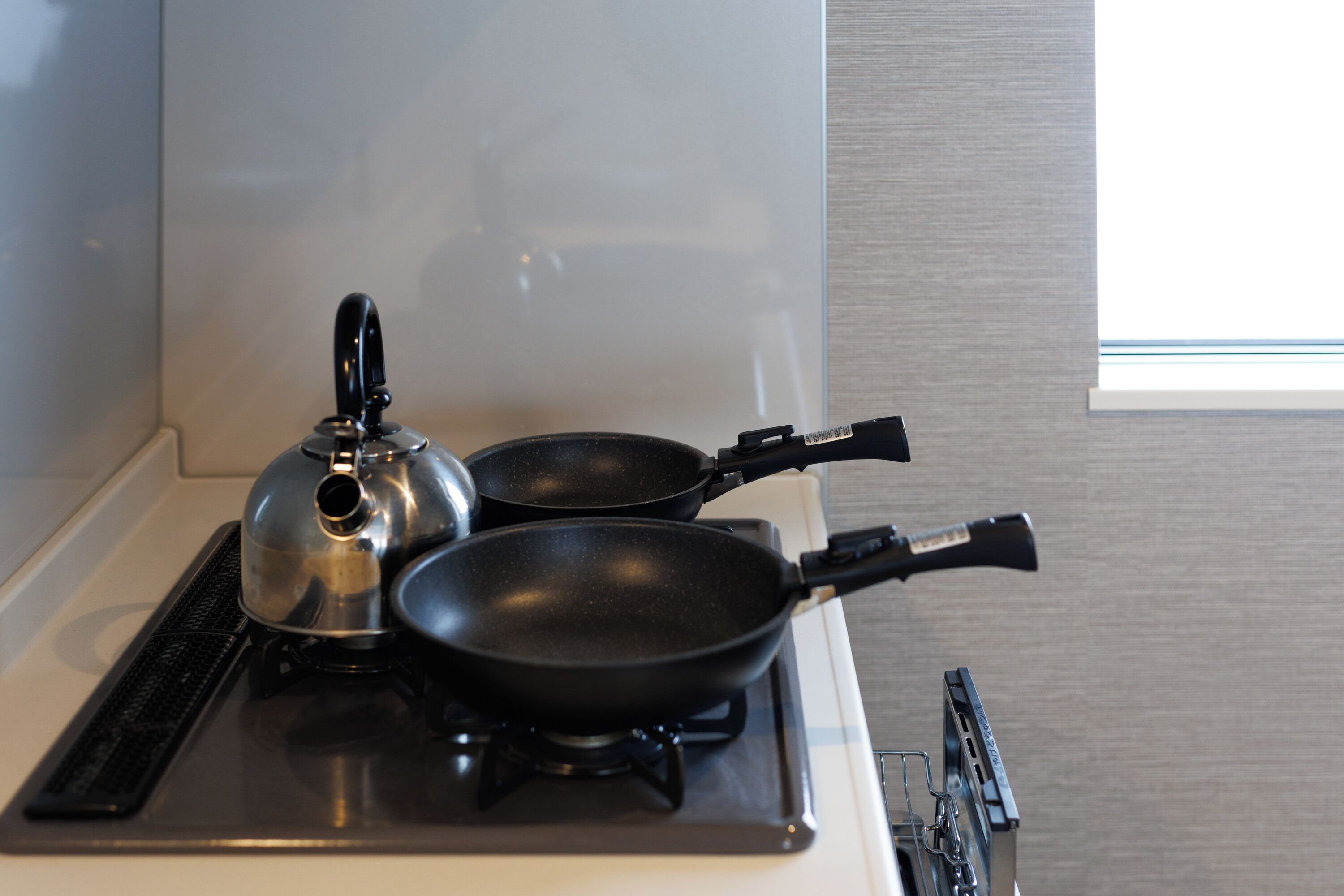 A kitchen with a stove, a kettle, and two frying pans.