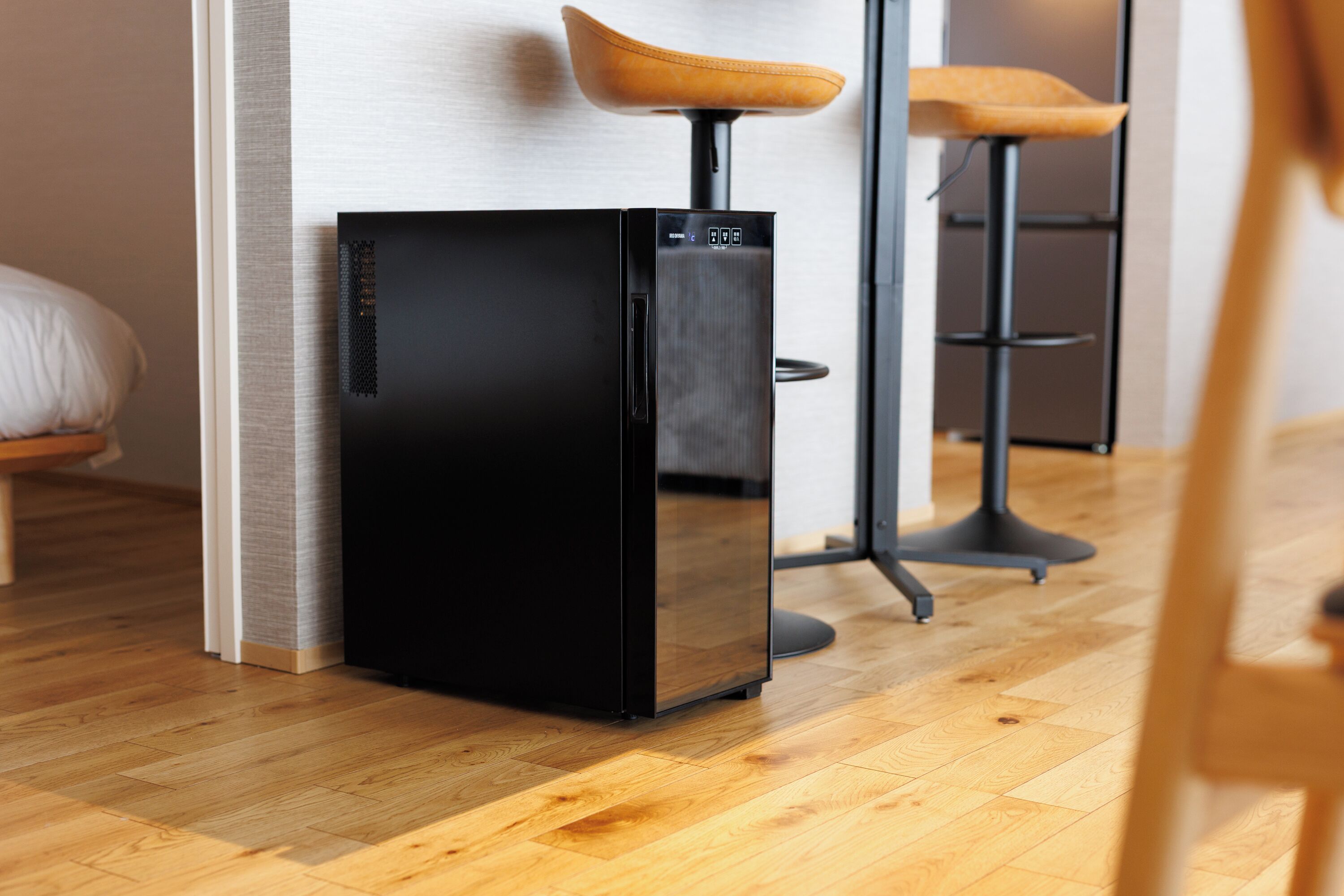Una cocina moderna con un refrigerador negro, piso de madera y un taburete de bar con asiento de cuero.