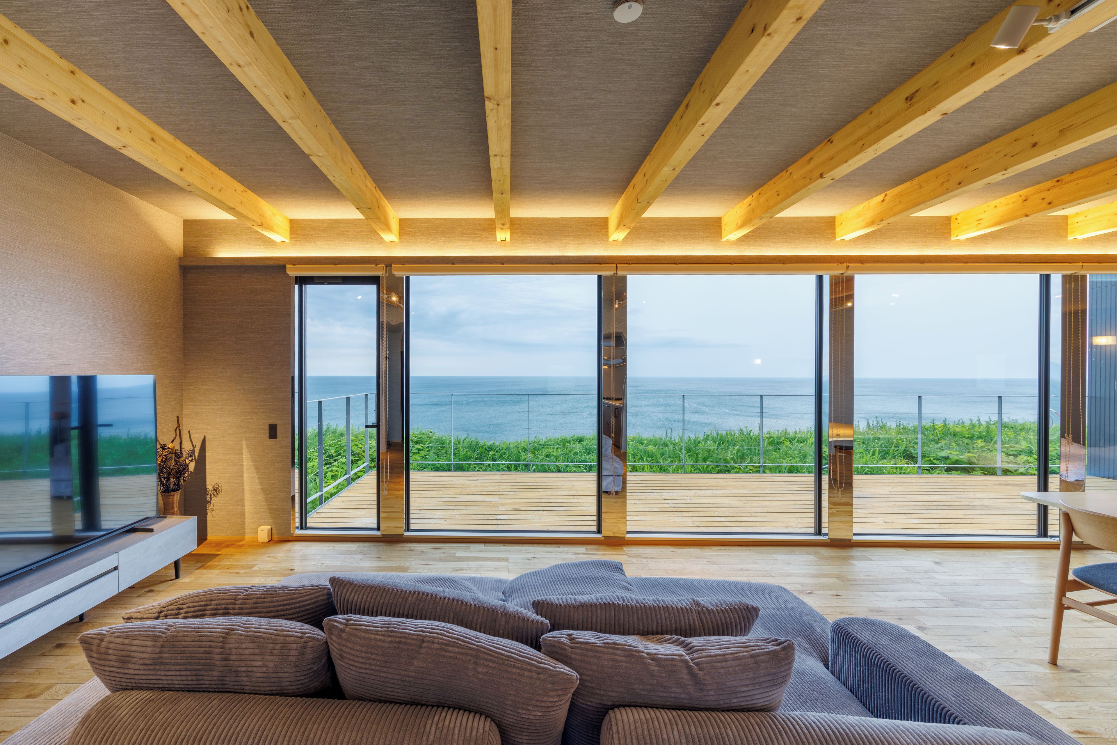 Un intérieur moderne avec un grand canapé, un plancher en bois et une vue sur la mer grâce à de grandes portes vitrées.