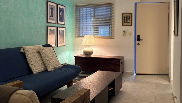 A living room with a blue sofa, a wooden bench, a lamp, and framed pictures on the wall. - Shelter among plants in Tampiquito 2br, 3bed, 2ba (San Pedro Garza García)