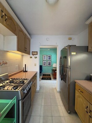 A kitchen with a gas stove, refrigerator, wooden cabinets, and a tiled floor.