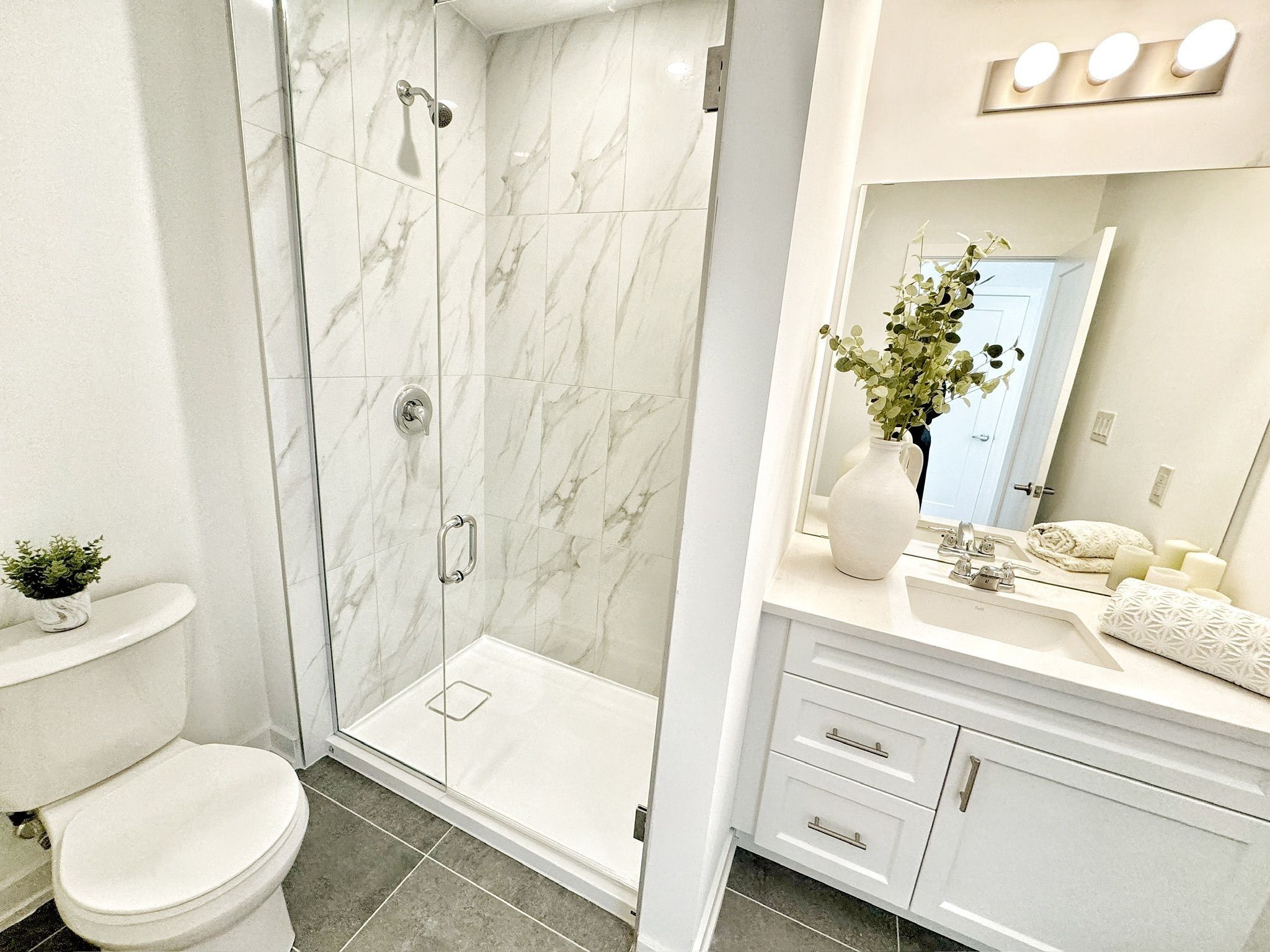 A modern bathroom with a glass-enclosed shower, a white toilet, and a vanity with a mirror and sink.