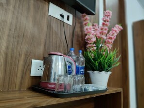 Una kitchenette con hervidor, vasos y botellas de agua sobre una encimera de madera.