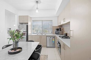 A modern kitchen with a dining area, featuring a marble table, black chairs, a refrigerator, a microwave, and a sink. - Best Location Armadale Sleeps 6 (Perth)