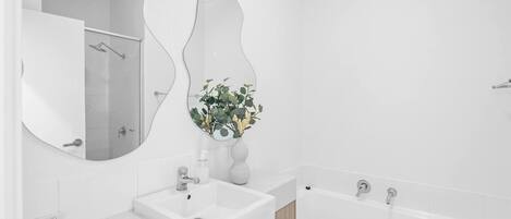 A modern bathroom with a large mirror, a sink, a shower, and a bathtub.