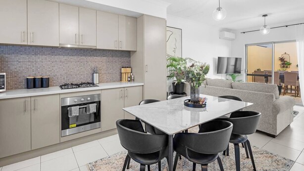 A modern kitchen with a dining area, featuring a large table, chairs, and a built-in oven. - Best Location Armadale Sleeps 6 (Perth)