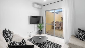 A modern living room with a flat-screen TV, a sofa set, a coffee table, and a sliding glass door leading to an outdoor patio. - Best Location Armadale Sleeps 6 (Perth)