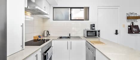 A modern kitchen with white cabinets, a stainless steel range, a microwave, and a window above the sink.