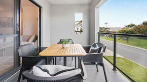 A balcony with a wooden table and black wicker chairs, a small potted plant, and a view of a street and greenery. - Stylish 2BR With Wi-fi 100 Mbps TV big 75 Inch (Perth)