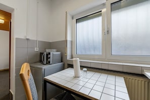 Une petite cuisine équipée d’un four à micro-ondes, d’un distributeur d’essuie-tout et d’une fenêtre avec des stores.