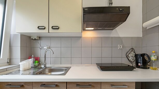 A modern kitchen with a sink, cabinets, a range hood, and a coffee maker.