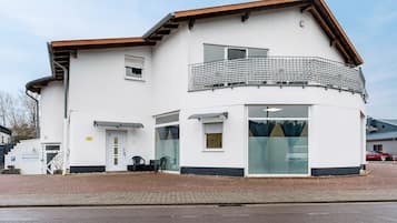 Un edificio a due piani con facciata bianca, un balcone con ringhiera in metallo e un ingresso a livello strada con porta e finestre.