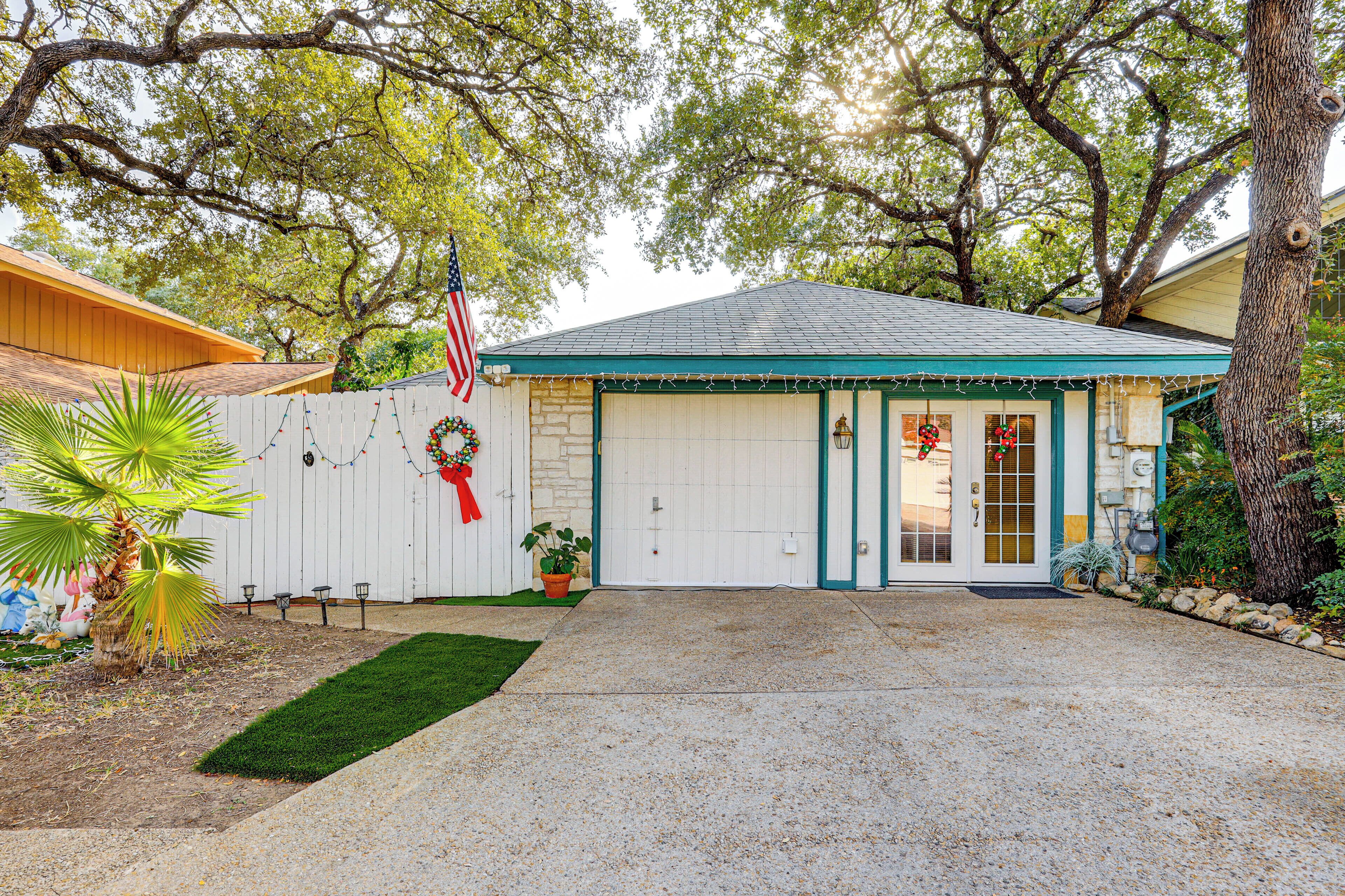 A house with a white garage door, a front porch, and a small garden with a palm tree.
