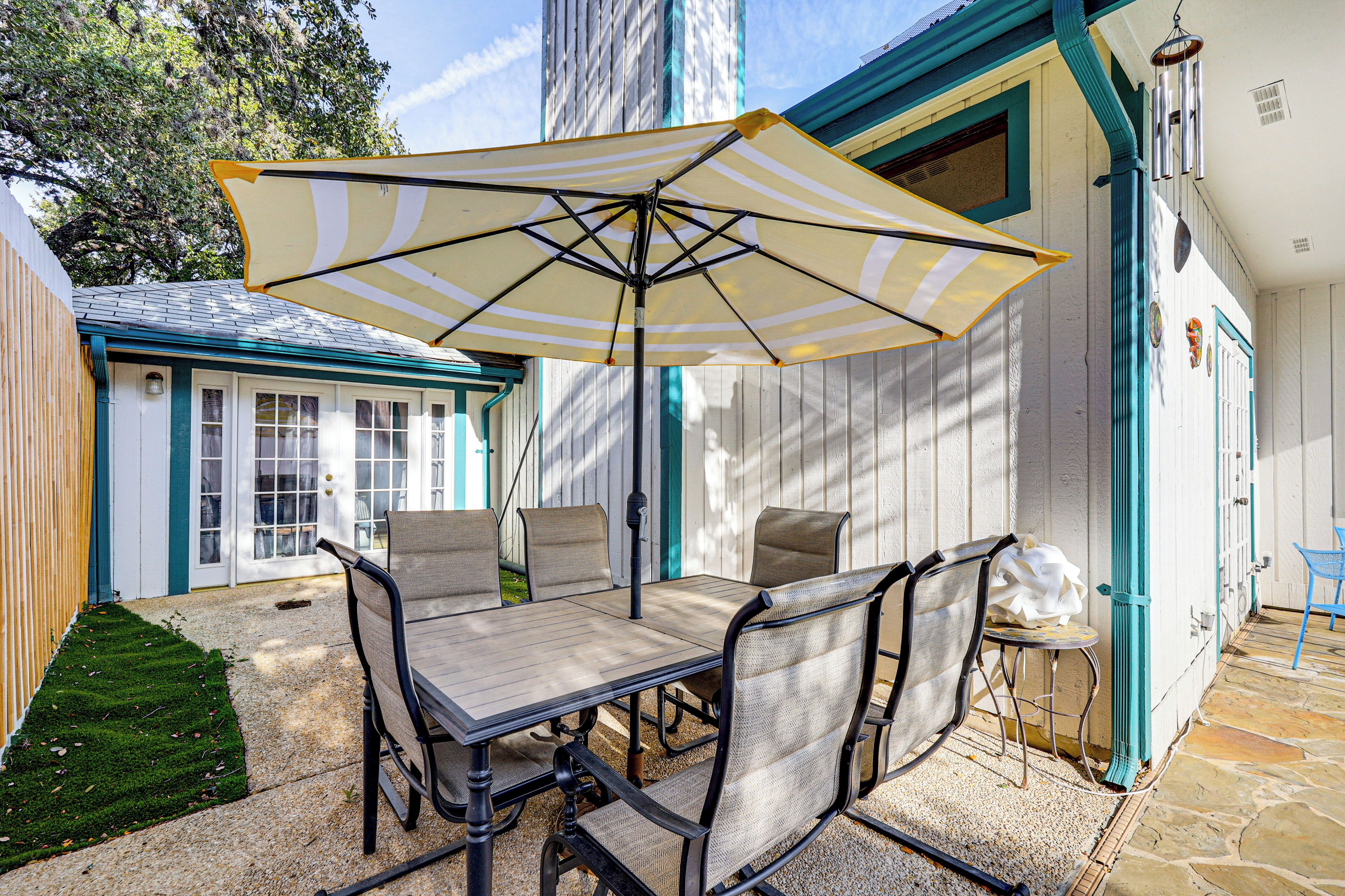 A patio with a table and chairs, an umbrella, and a small stool.