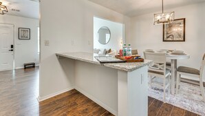 Una cucina moderna con un piano di lavoro in granito, un'area pranzo con sedie bianche e un lampadario.