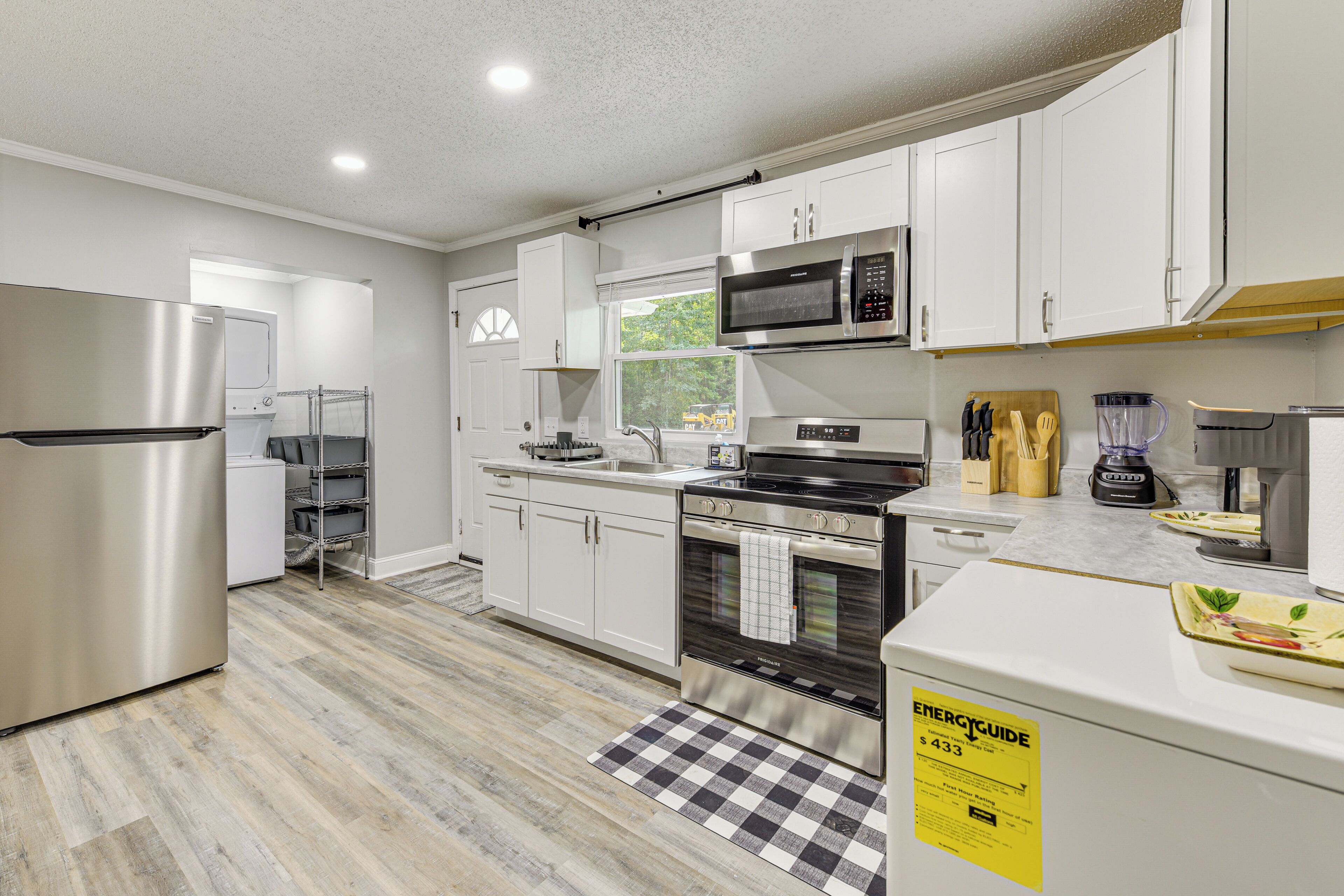 A modern kitchen with white cabinets, stainless steel appliances, and a checkered floor mat.
