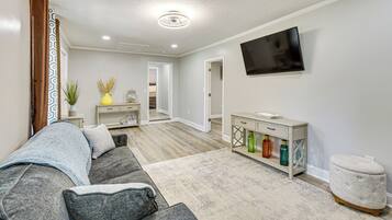 A modern living room with a grey sofa, a flat-screen TV mounted on the wall, and a wooden floor.