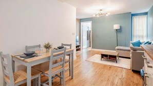 A modern living room with a dining area, wooden flooring, and a grey sofa.