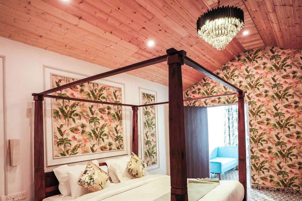 A four-poster bed with a canopy, a wooden ceiling, and patterned wallpaper.