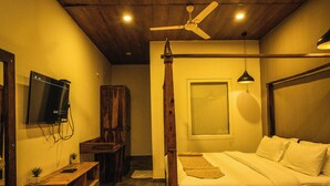 Un dormitorio con techo de madera, una cama con ropa de cama blanca, un ventilador de techo, un televisor montado y un armario de madera.
