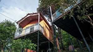 Una casa de dos pisos con un balcón en el nivel superior, rodeada de árboles.