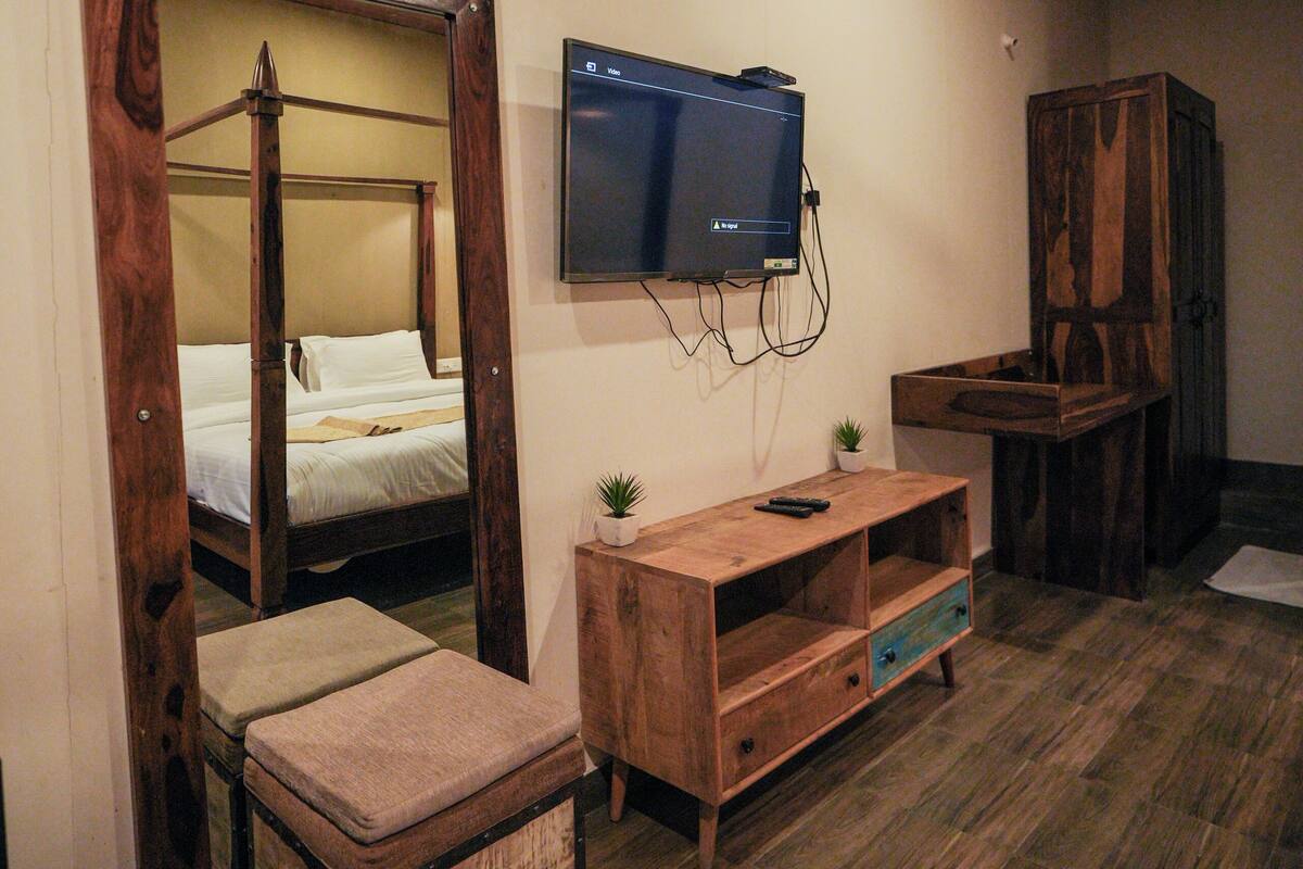 A bedroom with a wooden four-poster bed, a television mounted on the wall, a wooden cabinet, and a small plant on a wooden shelf.