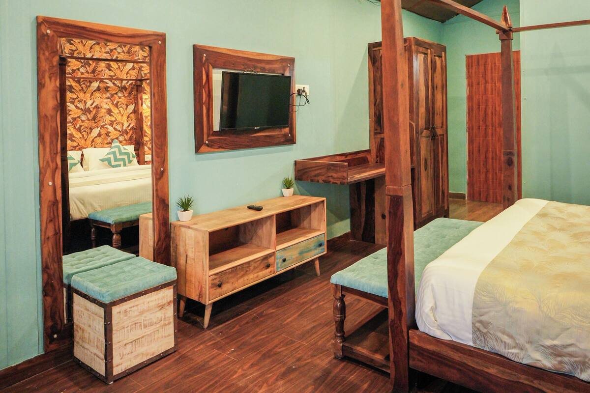 A bedroom with a wooden ceiling, a bed, a wooden bench, a TV, and a mirror.