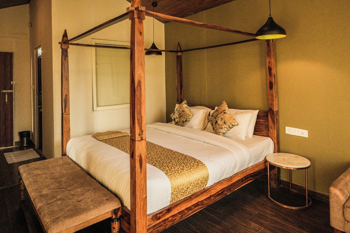 A four-poster bed with a wooden frame, a bench, a small round table, and a ceiling fan.