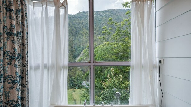 Un baño moderno con una bañera grande, una ventana con cortinas y vistas a un paisaje verde.