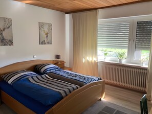 A bedroom with a wooden bed, a nightstand, a lamp, a radiator, and a window with blinds.