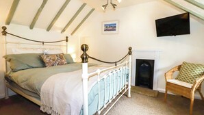 A bedroom with a bed, a chair, a fireplace, and a TV mounted on the wall. - Woodview (Looe)