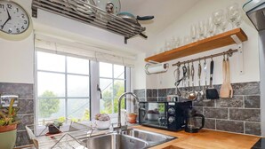 A modern kitchen with a stainless steel sink, a coffee maker, and a window with a view of greenery. - Woodview (Looe)