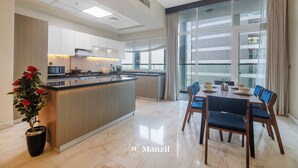 A modern kitchen with a central island, a dining area with a table and chairs, and a large window with a view of the city. - Manzil - Luxury 2BR w Pool and Burj View (Dubai)