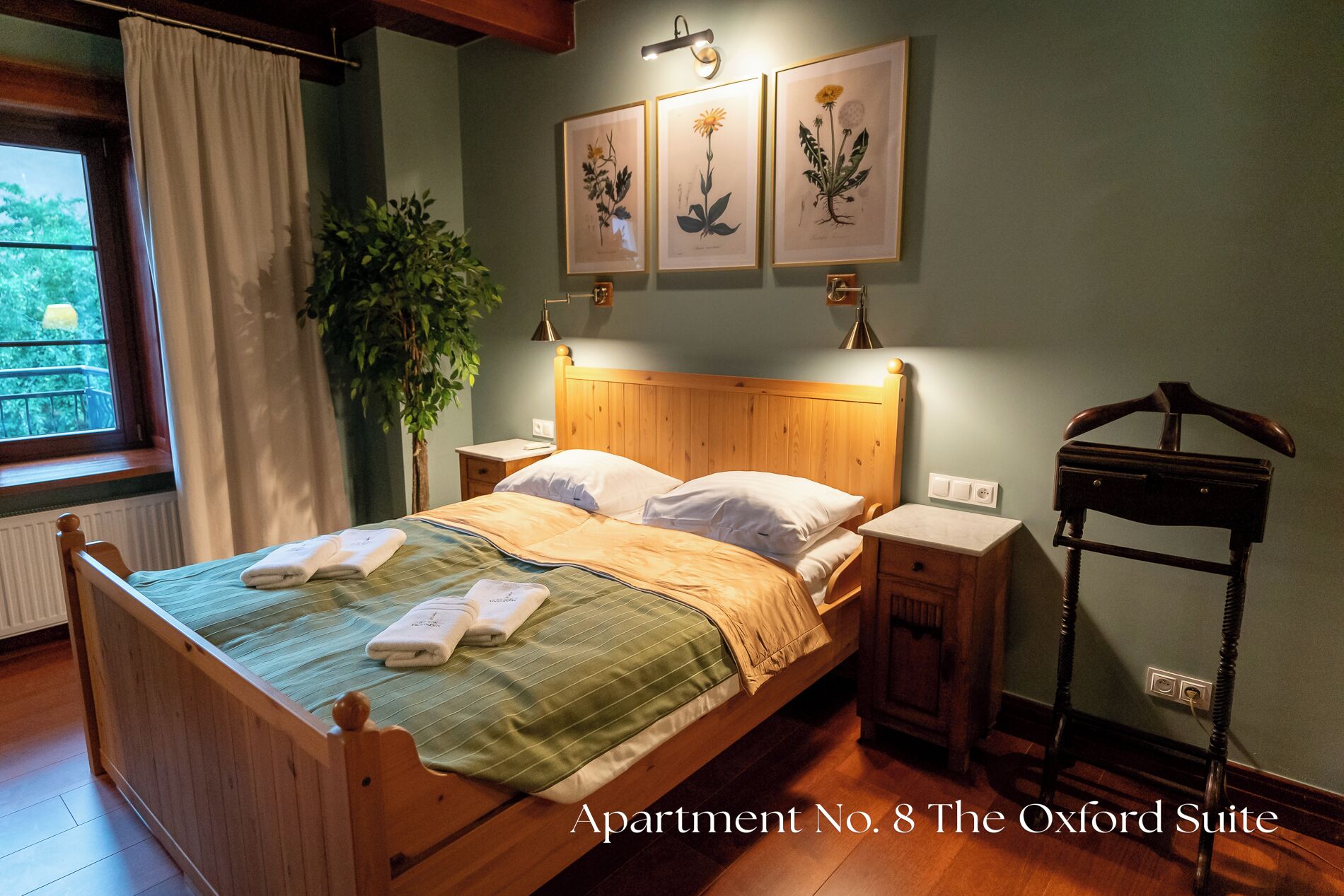 Une chambre à coucher avec un lit en bois, une table de chevet, une lampe, une plante et des reproductions botaniques encadrées accrochées au mur.