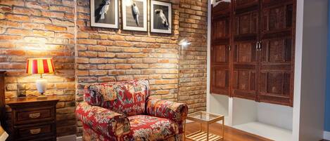 A room with a brick wall, a patterned armchair, a wooden cabinet, and framed artwork.