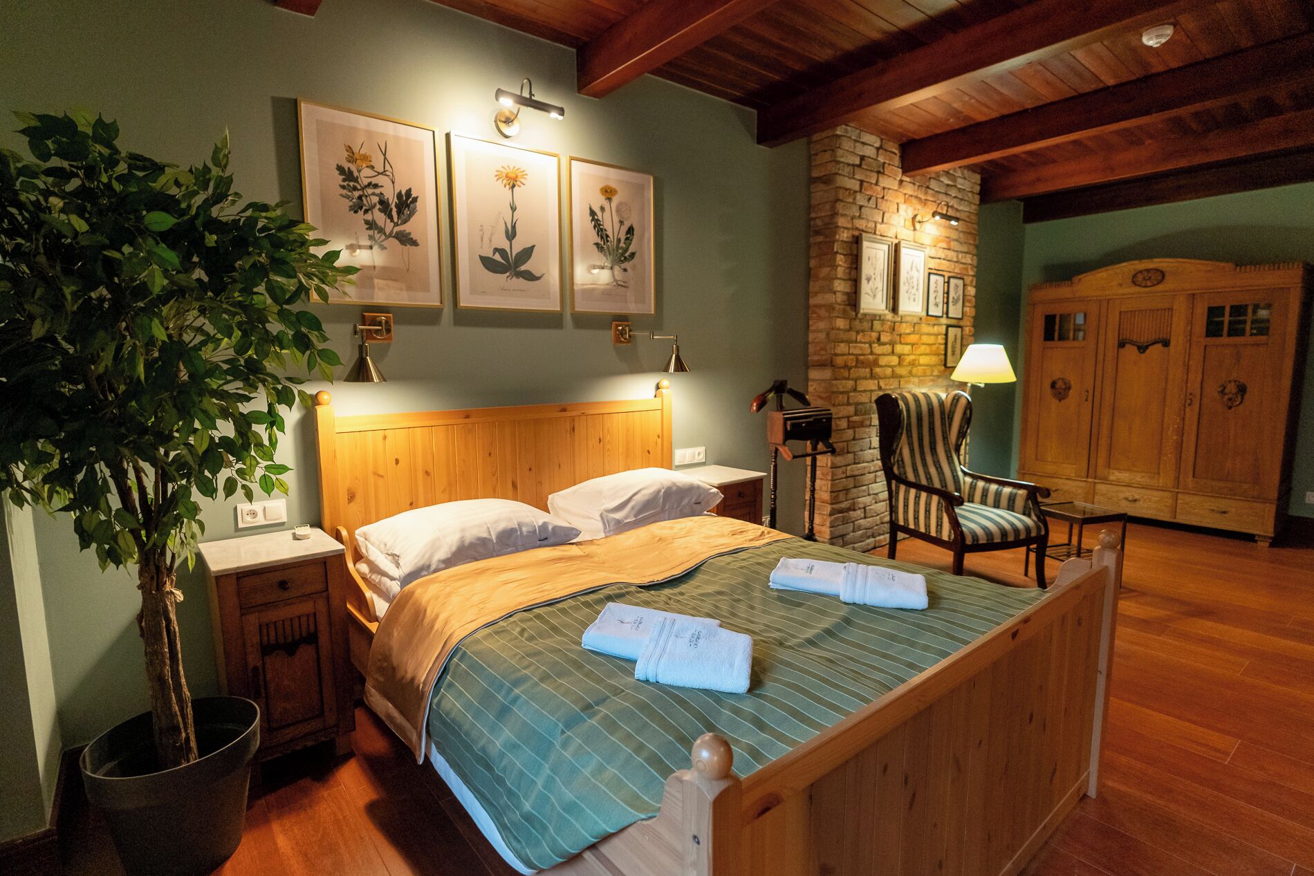 A neatly arranged bedroom with a wooden bed, a nightstand, a potted plant, and a stone wall.